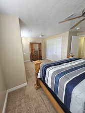 Carpeted bedroom featuring a textured ceiling, ceiling fan, and a closet