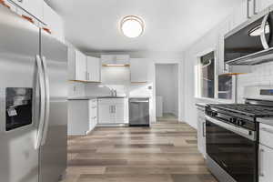 Kitchen featuring appliances with stainless steel finishes, white cabinets, tasteful backsplash, and light wood-style flooring