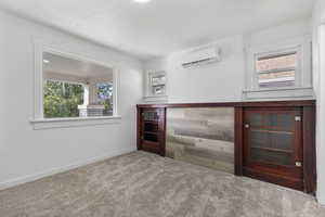 Unfurnished bedroom with multiple windows, carpet flooring, and a wall unit AC
