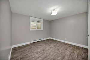 Unfurnished bedroom with wood finished floors and a baseboard radiator