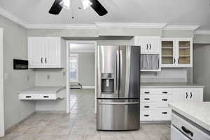 Kitchen featuring stainless steel fridge with ice dispenser, crown molding, light countertops, white cabinetry, and light tile patterned floors
