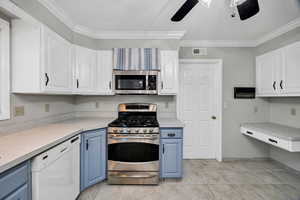 Kitchen with white cabinets, stainless steel appliances, light countertops, crown molding, and blue cabinets