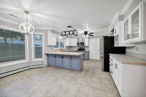 Kitchen with white cabinetry, blue cabinetry light countertops, hanging light fixtures, crown molding, and a peninsula