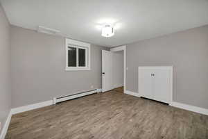 Unfurnished bedroom with attic access, a baseboard radiator, and light wood finished floors
