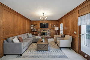Virtually Staged Carpeted living area featuring wooden walls, a brick fireplace, ornamental molding, built in features, and a chandelier