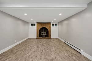 Unfurnished downstairs family room featuring a baseboard heating unit, recessed lighting, light wood finished floors, and a wood stove
