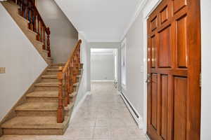 Entryway featuring a baseboard heating unit, ornamental molding, stairs, and light tile patterned floors