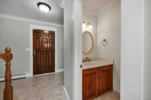 Half bath with ornamental molding, light tile patterned floors, vanity, a textured ceiling, and baseboard heating