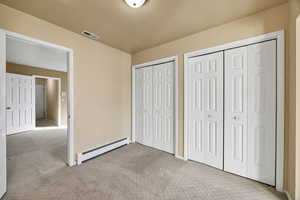 Unfurnished upstairs bedroom featuring two closets, a baseboard radiator, light colored carpet, and a textured ceiling