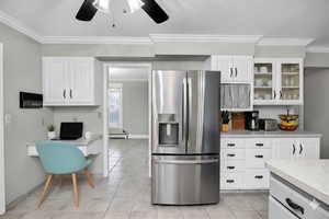 Virtually Staged Kitchen with built in study area, stainless steel fridge with ice dispenser, light countertops, ornamental molding, and white cabinets