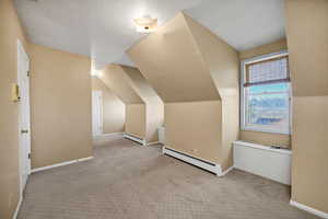 Upstairs Bedroom with a textured ceiling, light carpet, baseboard heating, and vaulted ceiling