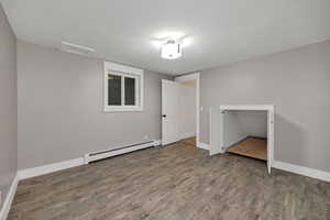 Unfurnished bedroom featuring baseboard heating, wood finished floors, and attic access