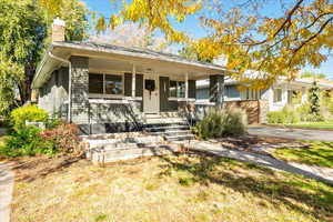 View of front of house featuring covered porch, a chimney, brick siding, driveway, and a garage