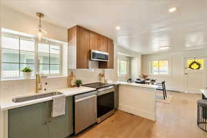 Kitchen with backsplash, decorative light fixtures, appliances with stainless steel finishes, light wood-style floors, and a peninsula