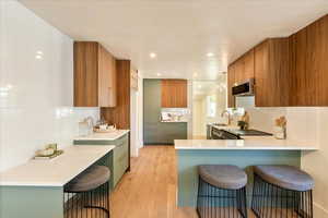 Kitchen with a kitchen breakfast bar, light wood-style floors, a peninsula, decorative backsplash, and stainless steel appliances