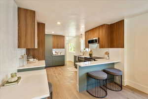 Kitchen featuring light wood-style floors, brown cabinetry, tasteful backsplash, a breakfast bar, and appliances with stainless steel finishes