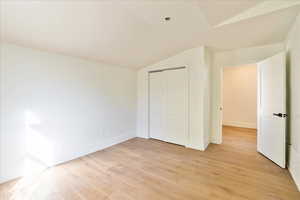 Unfurnished bedroom with vaulted ceiling, light wood finished floors, and a closet