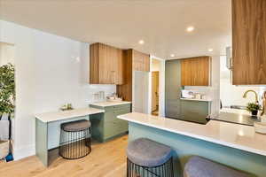Kitchen with a breakfast bar area, light wood finished floors, green cabinets, recessed lighting, and decorative backsplash