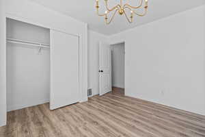 Unfurnished bedroom featuring light wood finished floors, a chandelier, and a closet