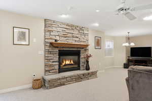 Living room with light carpet, a stone fireplace, a ceiling fan, and recessed lighting