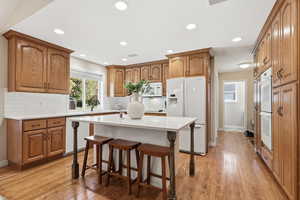 Kitchen featuring brown cabinets, a breakfast bar area, white appliances, light wood-style flooring, and recessed lighting