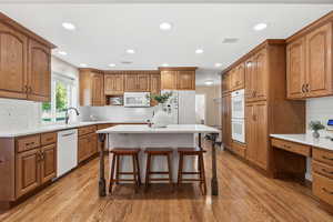 Kitchen with brown cabinetry, backsplash, white appliances, light wood-style floors, and recessed lighting