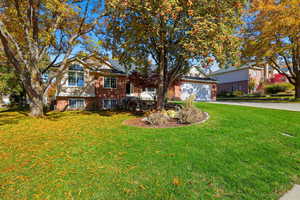 View of front of property with brick siding, a front yard, driveway, and an attached garage