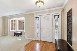 Foyer with crown molding, plenty of natural light, wood finished floors, and carpet floors