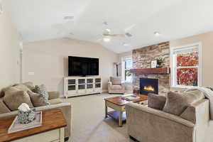 Carpeted living room with a fireplace, lofted ceiling, and a ceiling fan