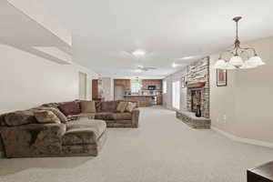 Living room with light carpet, a chandelier, a stone fireplace, and ceiling fan