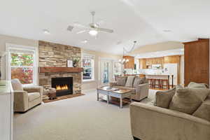 Living room featuring a chandelier, a fireplace, light carpet, a ceiling fan, and lofted ceiling