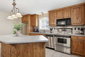 Kitchen with stainless steel appliances, light countertops, brown cabinets, and backsplash