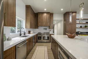 Kitchen with light stone countertops, light wood finished floors, appliances with stainless steel finishes, hanging light fixtures, and recessed lighting