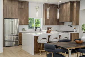 Kitchen with high end fridge, a breakfast bar, light wood finished floors, pendant lighting, and light stone countertops