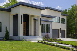 Contemporary home with stucco siding, driveway, a front lawn, a porch, and an attached garage