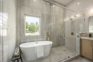 Full bathroom with tile walls, a freestanding bath, a stall shower, and vanity
