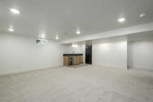 Below grade area featuring bar with sink, light carpet, recessed lighting, and wine cooler