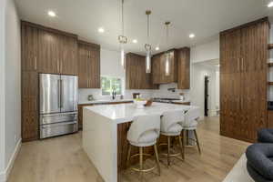 Kitchen featuring a kitchen breakfast bar, high end fridge, brown cabinets, light wood-style floors, and recessed lighting