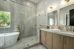 Full bathroom with tile walls, a freestanding tub, double vanity, a shower stall, and light tile patterned flooring