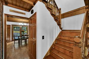 Staircase featuring a chandelier, wood-type flooring, and a wood ceiling with exposed beams