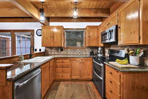 Kitchen featuring stainless steel appliances, dark wood-style floors, brown cabinetry, a peninsula, and a wooden ceiling with exposed beams