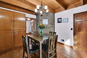 Dining area with dark wood-style floors, a chandelier, and a wooden ceiling with exposed beams