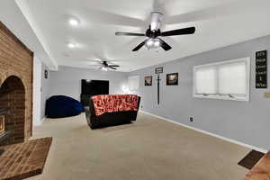 Living area featuring a brick fireplace, carpet flooring, and a ceiling fan