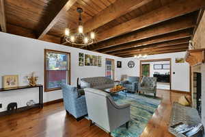 Living area featuring a chandelier, a fireplace, wood finished floors, and a wooden ceiling with exposed beams
