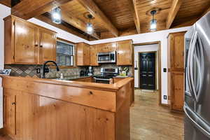 Kitchen featuring stainless steel appliances, tasteful backsplash, a peninsula, brown cabinetry, and light wood-type flooring
