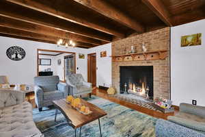 Living area with wood finished floors, a brick fireplace, beamed ceiling, and a chandelier