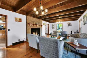 Living room with a chandelier, wood finished floors, a brick fireplace, and a wood ceiling with exposed beams