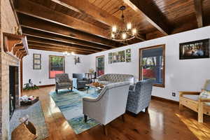 Living room with a chandelier, a brick fireplace, beam ceiling, and wood finished floors