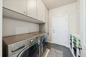 Washroom with cabinet space, separate washer and dryer, dark colored carpet, and a textured ceiling