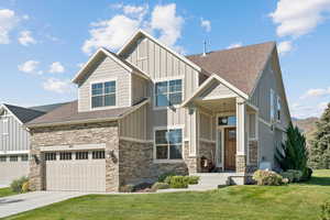 Craftsman house with board and batten siding, roof with shingles, a front lawn, and stone siding